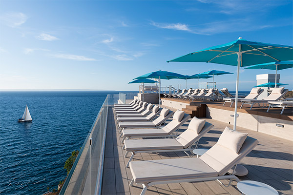 Vista de tumbonas en la terraza de la piscina infinity con vistas al mediterráneo y barco de fondo